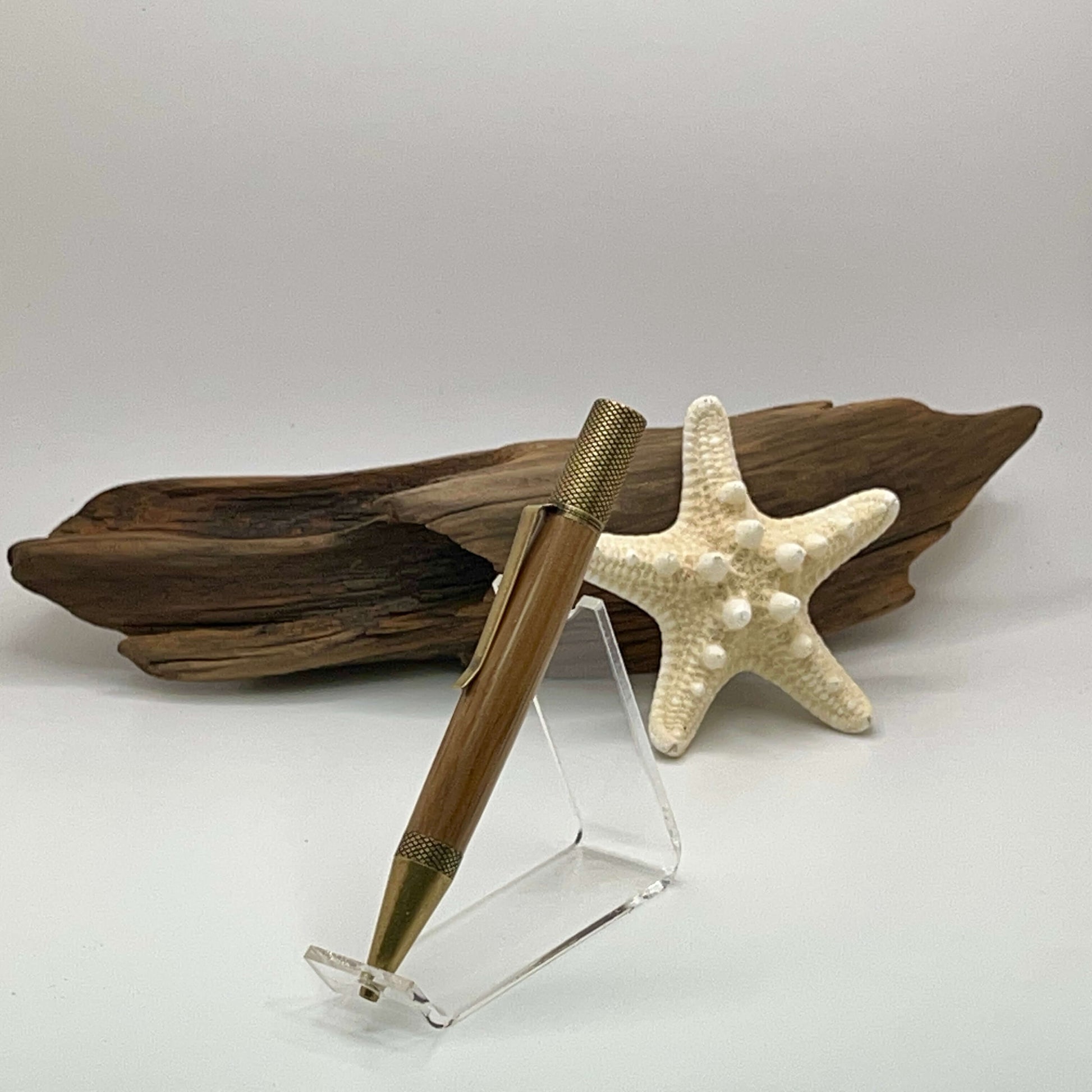 Exemplar antique brass ballpoint twist pen standing in frot of driftwood and starfish