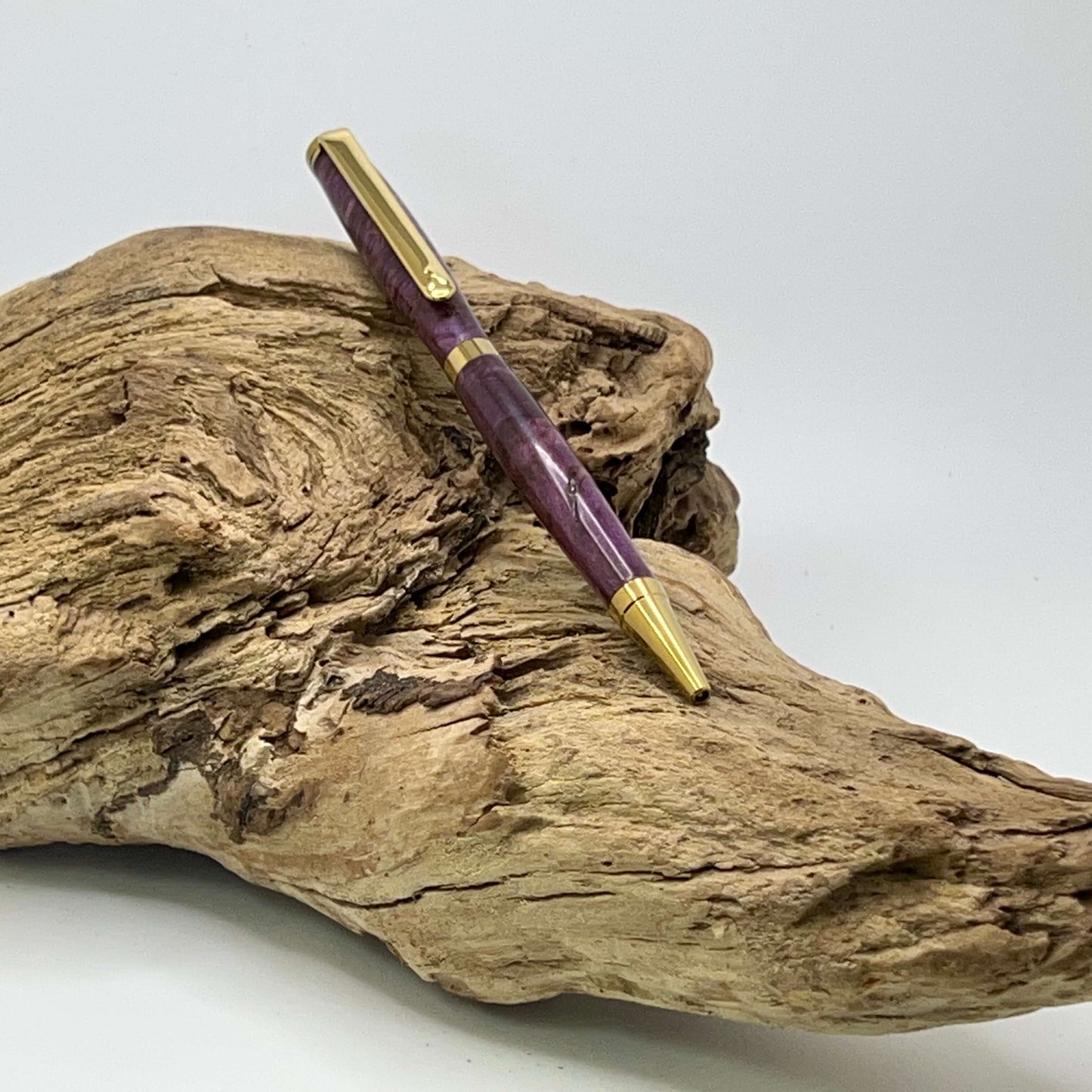 Handcrafted Box elder wood pen dyed purple setting on driftwood