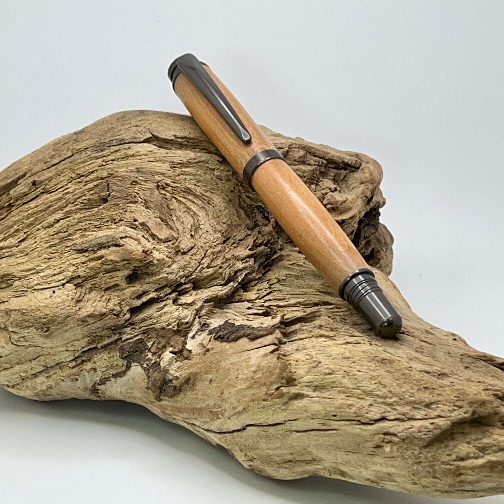 Handcrafted pen with cherry wood and satin gunmetal hardware setting on driftwood