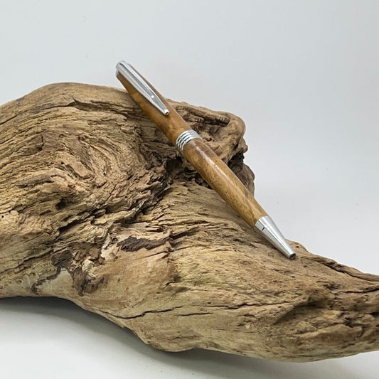 Handcrafted pen with Teak wood and Chrome hardware sitting on driftwood