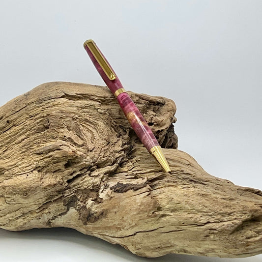 Handcrafted Box elder wood pen dyed magenta setting on driftwood